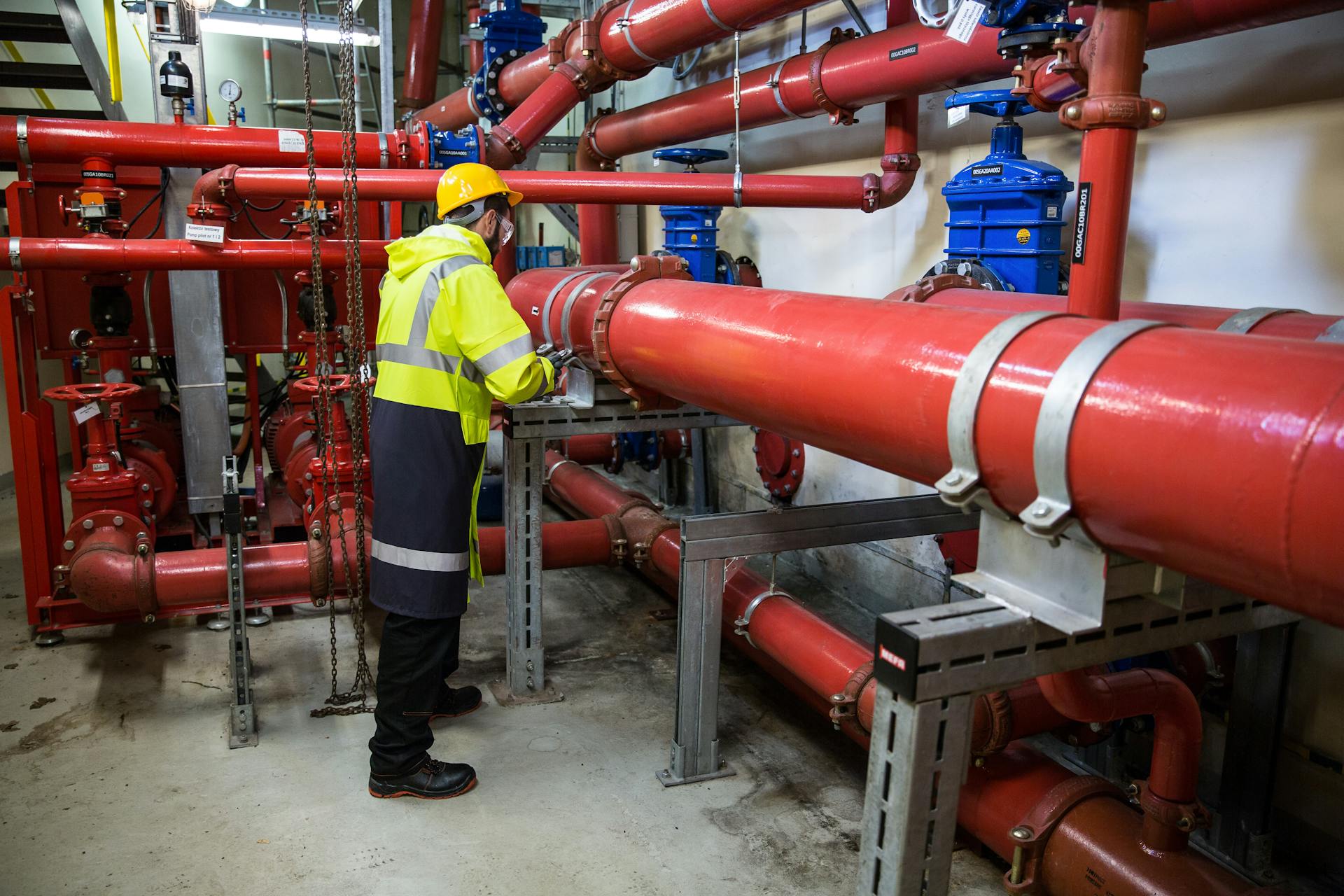 Engineer with safety gear inspecting red industrial piping system indoors.