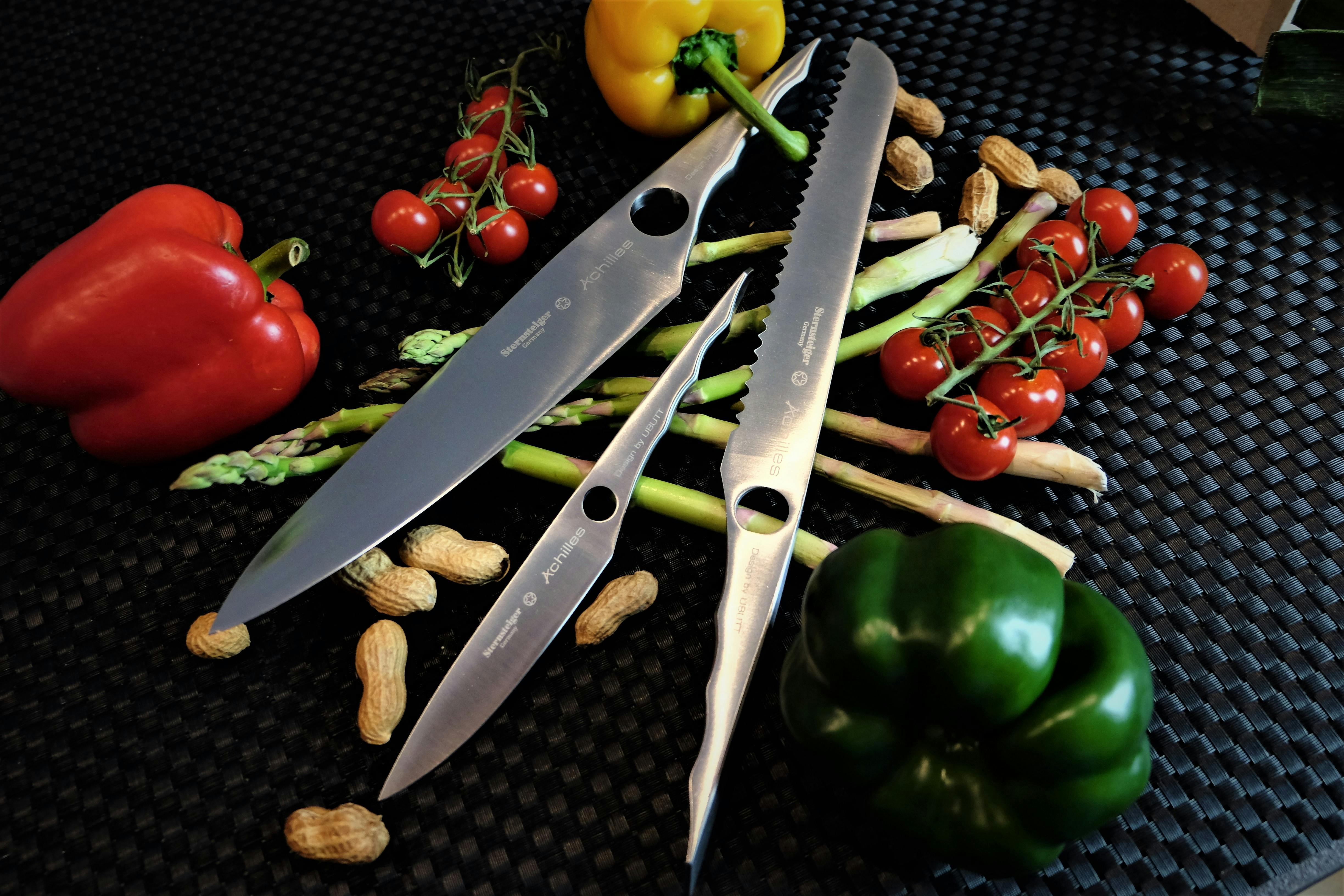 Free A collection of chef's knives with peppers, tomatoes, and peanuts on a black surface. Stock Photo
