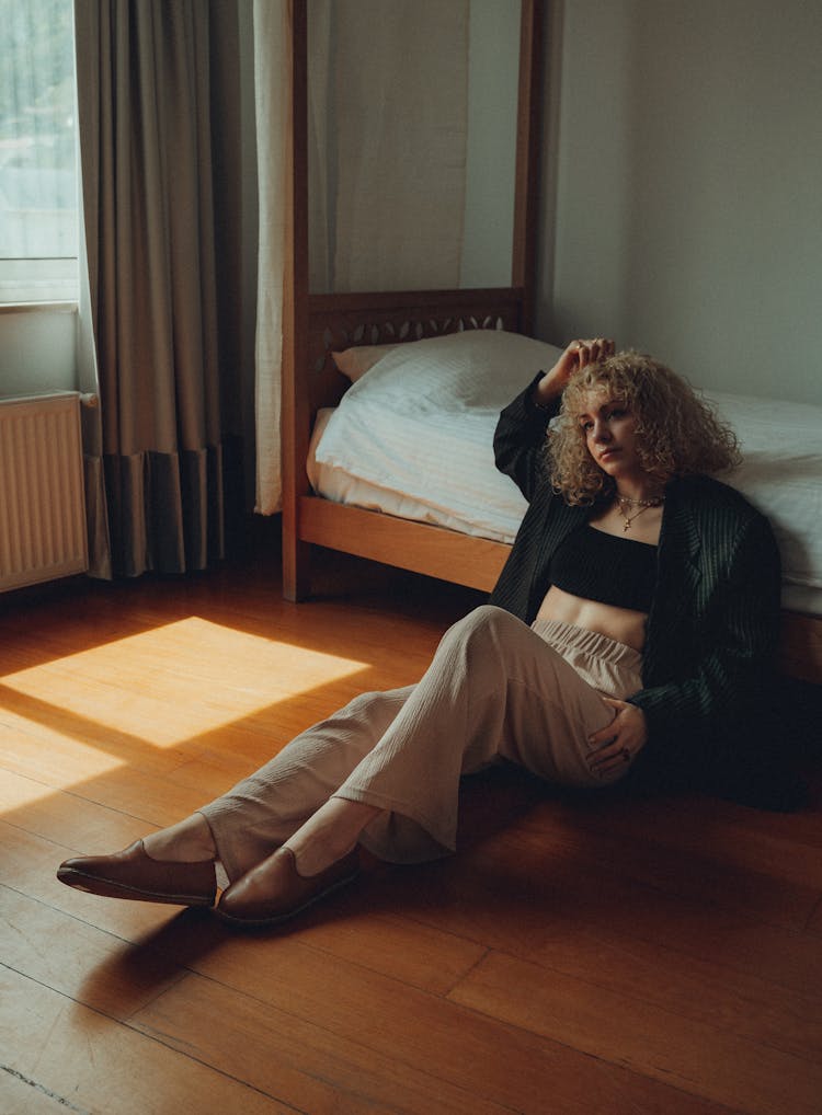 Young Fashionable Woman Sitting On The Floor Leaning Against The Bed 