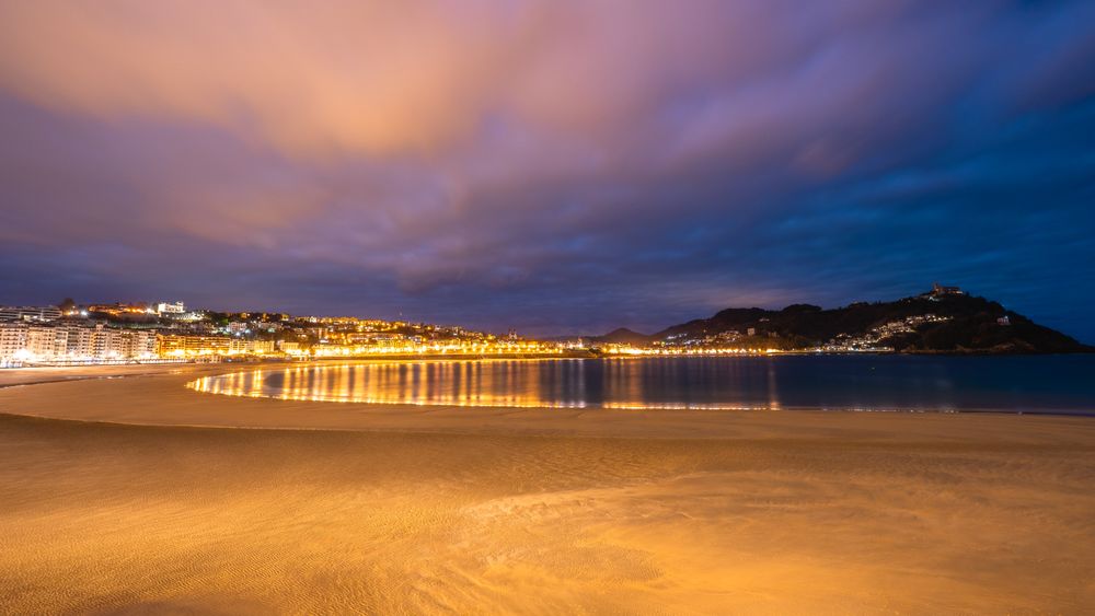 Playa de la Concha en San Sebastián con luces de la ciudad reflejadas al ocaso