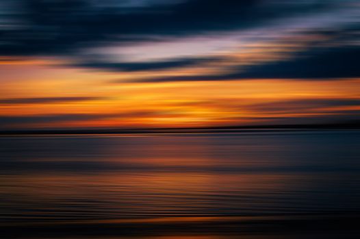 Blurred ocean sunset with vibrant orange and blue hues, capturing a serene seascape.