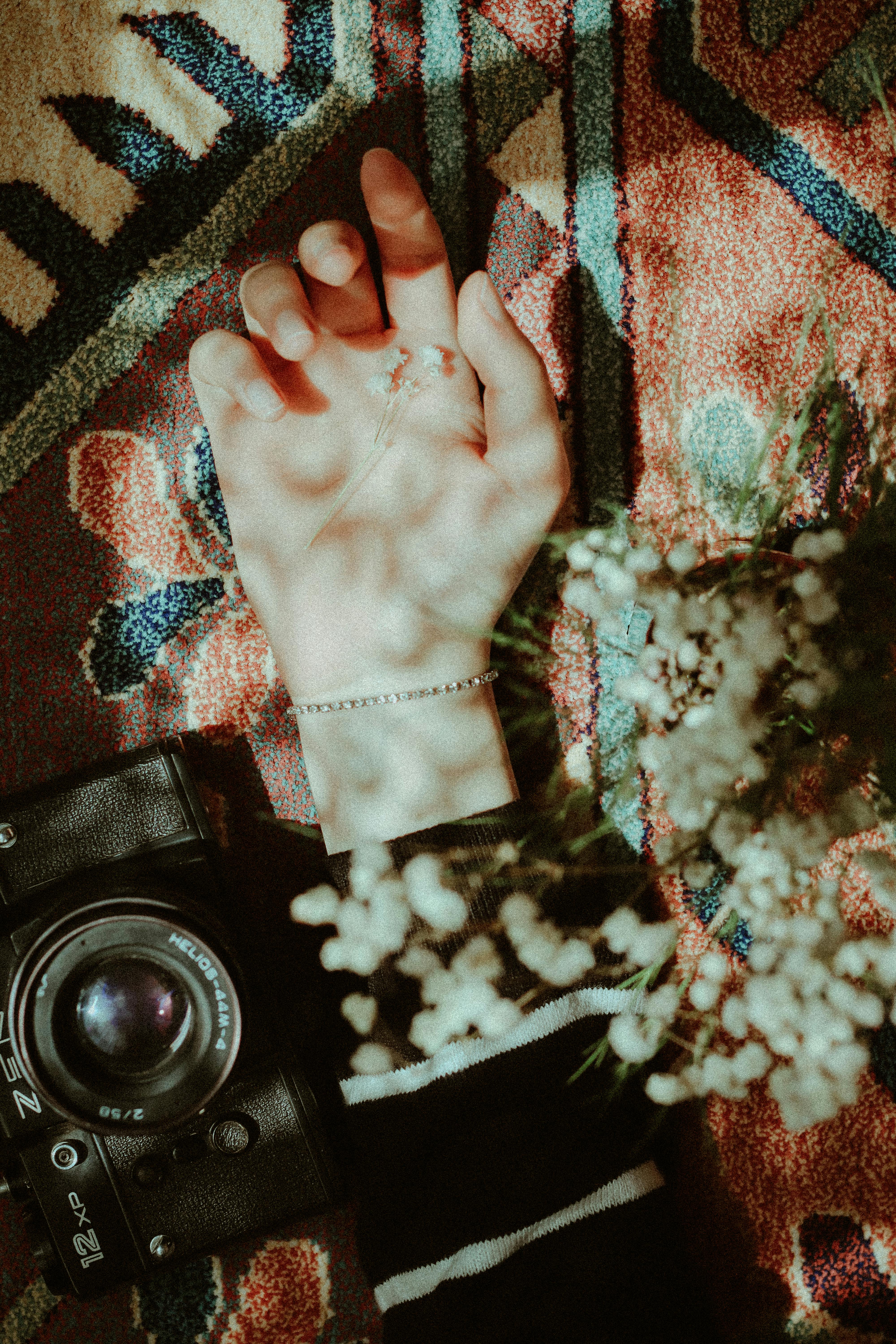 Close-up artistic shot of a hand resting on a patterned rug with flowers and a vintage camera.