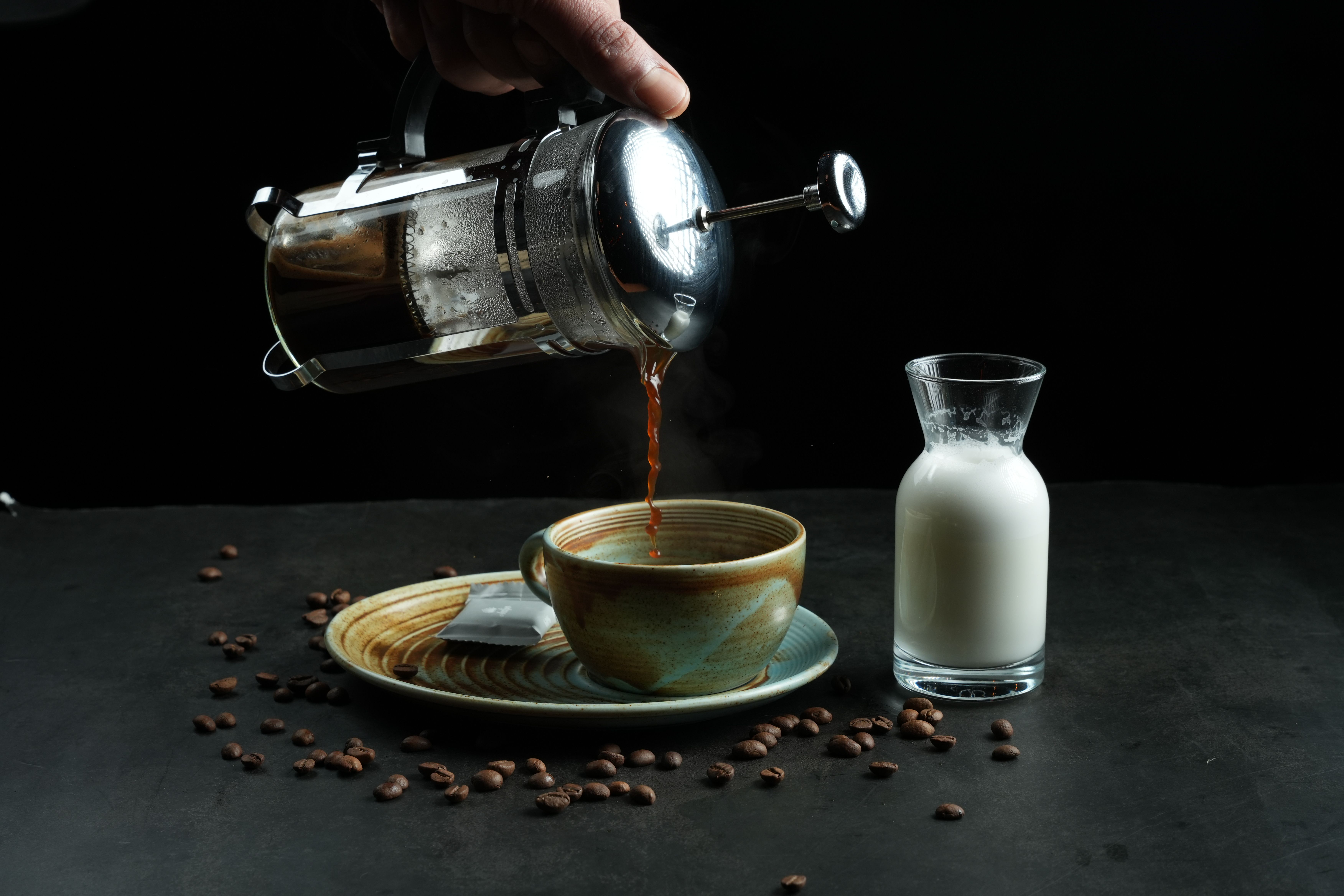 glass French press with fresh coffee on a kitchen counter next to a mug