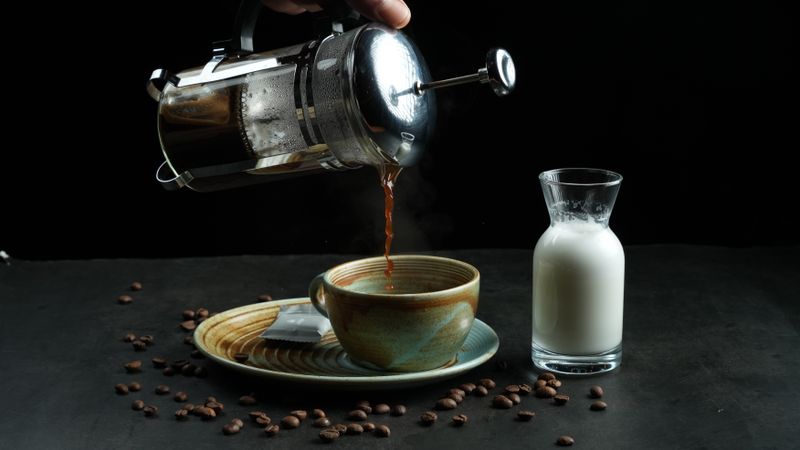 glass French press with fresh coffee on a kitchen counter next to a mug