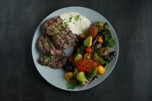 A top view of grilled beef steak with mixed vegetables and sauce on a plate.