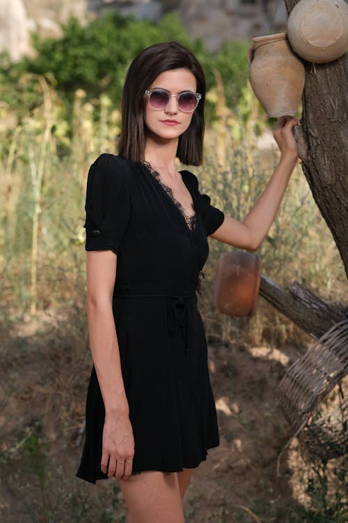 Portrait of a Pretty Brunette Wearing Sunglasses and a Black Dress Posing Outdoors