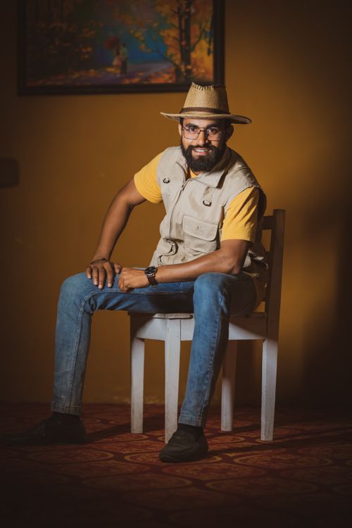 Free Portrait of a bearded man with eyeglasses and cowboy hat sitting on a chair indoors, depicting a casual modern style. Stock Photo