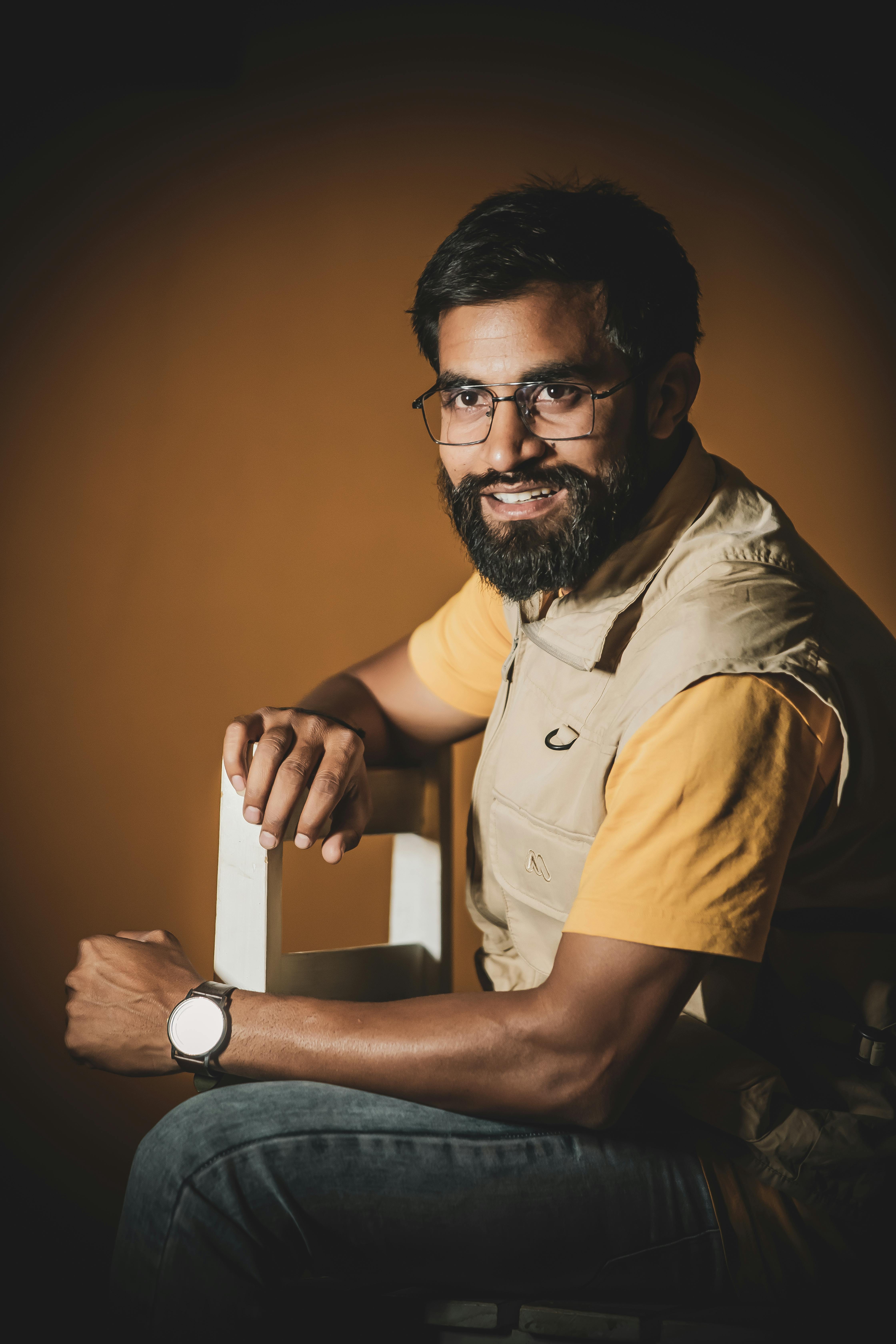 Portrait of a smiling bearded man in glasses, sitting indoors in a studio setting.