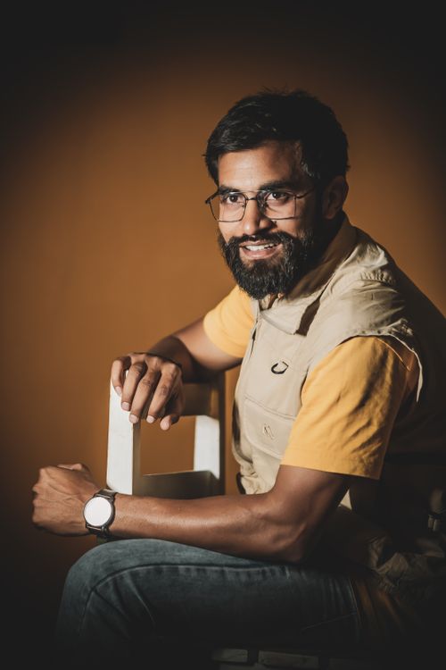 Free Portrait of a smiling bearded man in glasses, sitting indoors in a studio setting. Stock Photo
