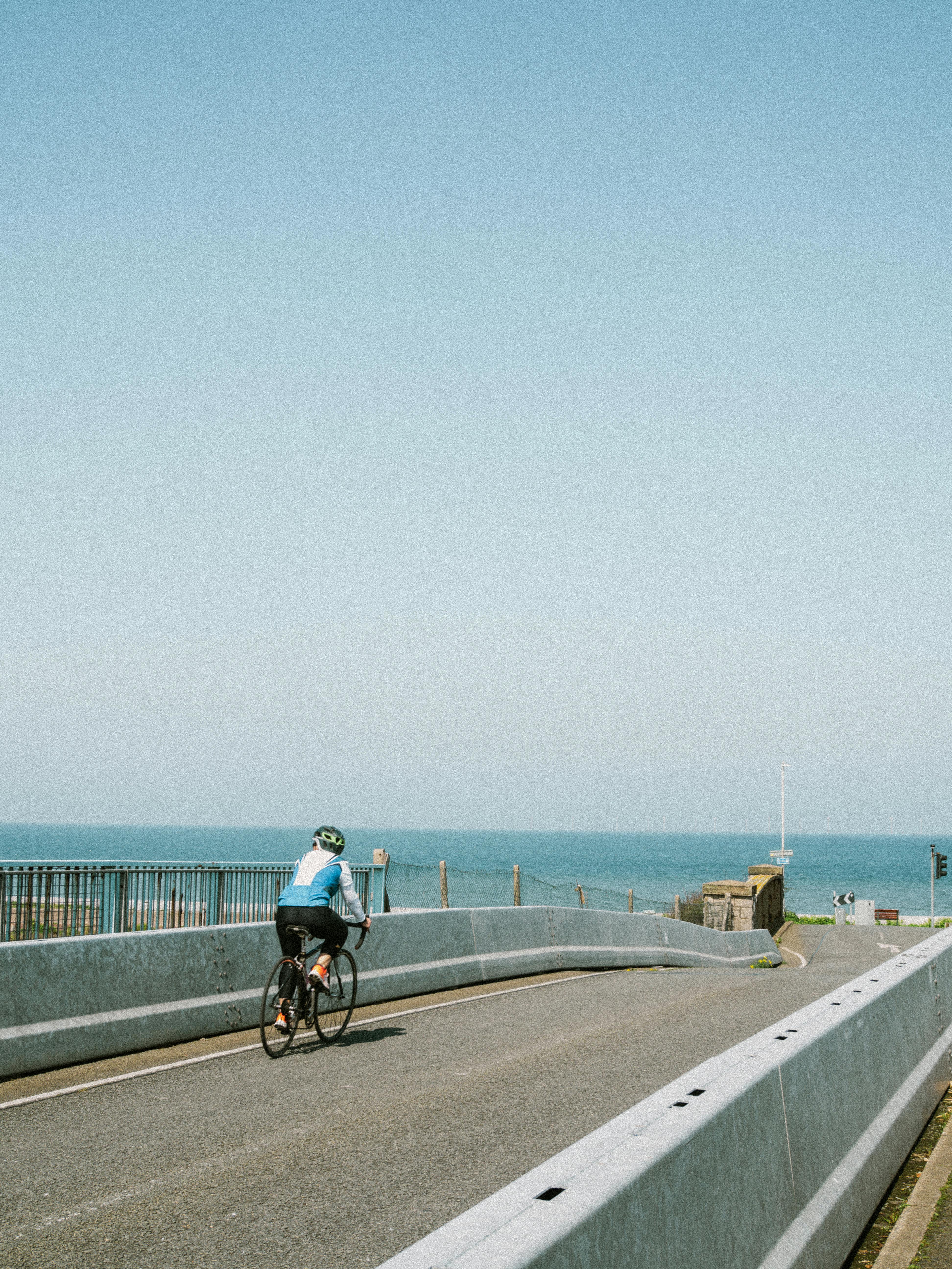 A cyclist rides along a coastal road with a clear view of the ocean under a blue sky, capturing the essence of a summer day.