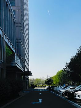 View of a city street with parked cars and a modern building under a clear blue sky.