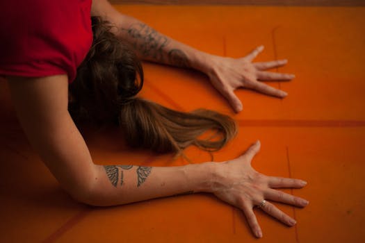 Close-up of a woman with tattoos practicing yoga on an orange mat.