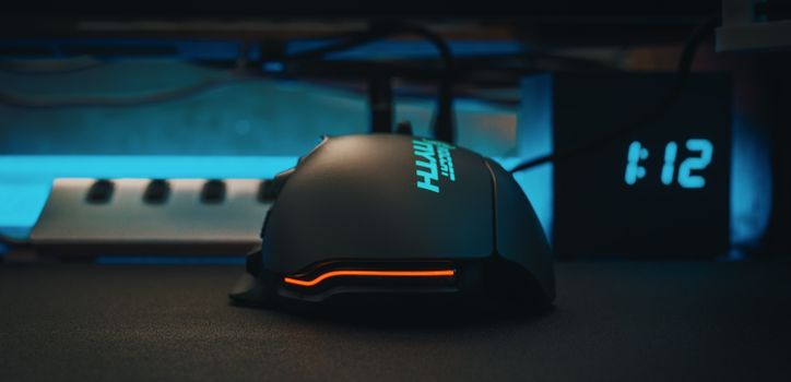 Modern computer mouse for users of massively multiplayer online role playing game placed on table against electronic clock