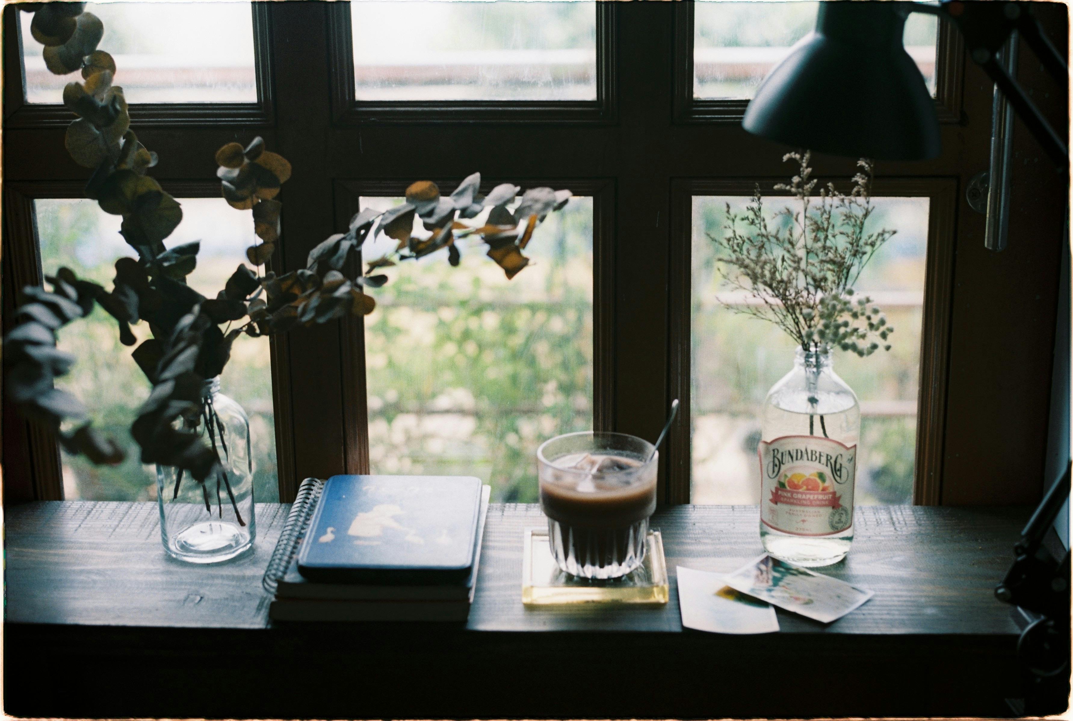 A serene still life of a drink, vase, and books on a windowsill.