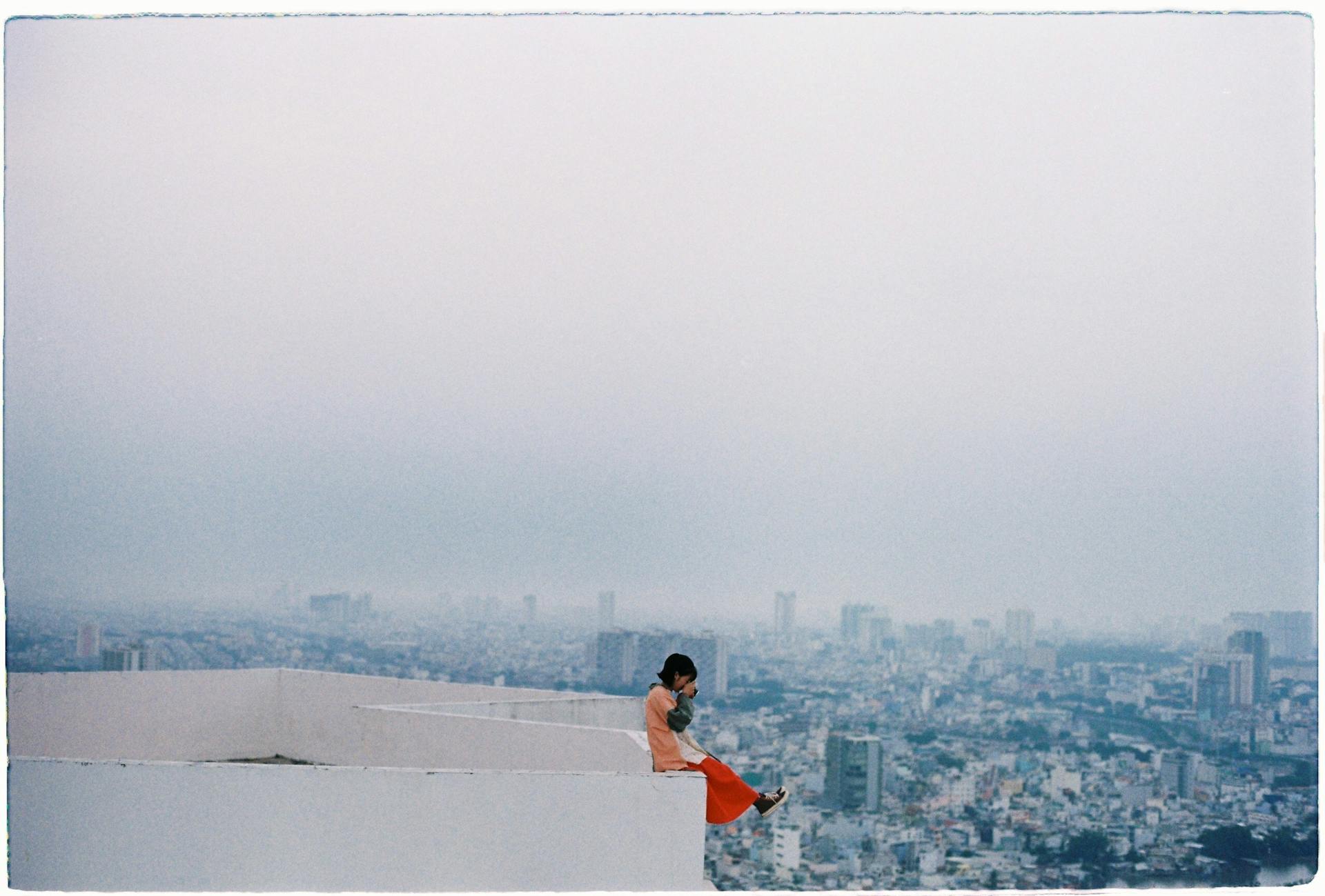 Woman Sitting on Top of a Skyscraper and Taking a Picture