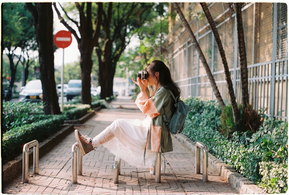A young woman captures moments with her camera, sitting on an urban sidewalk in summer.