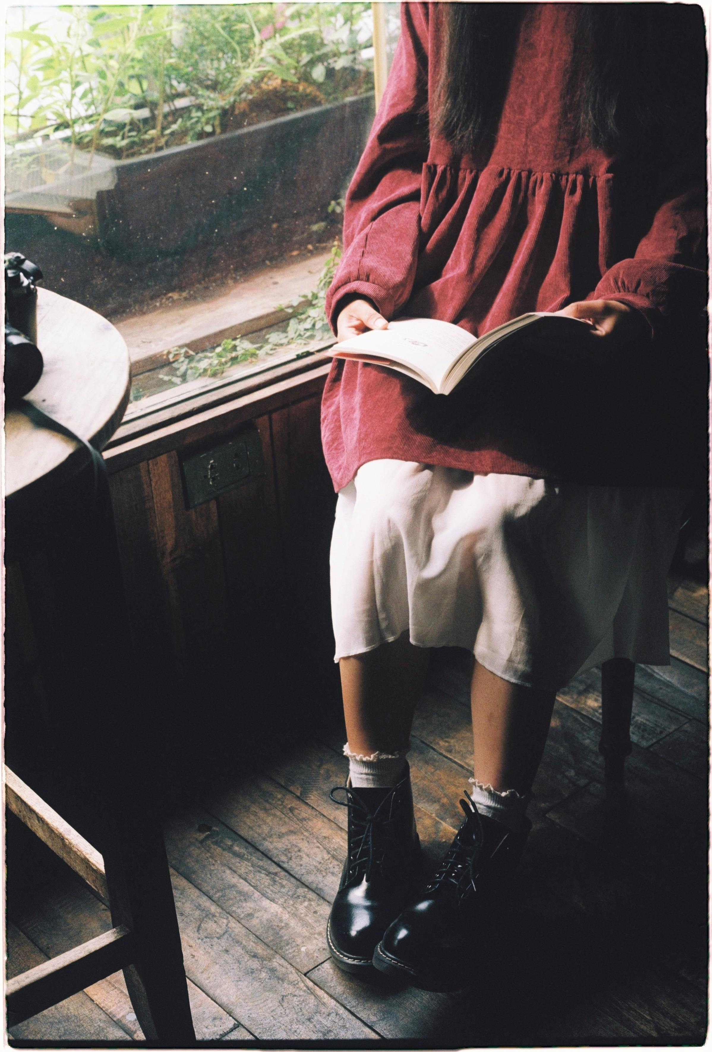 A woman in a vintage outfit reading a book indoors by a window.