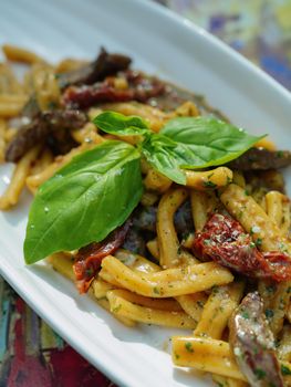 Tasty Italian pasta dish with pesto, sun-dried tomatoes, and fresh basil garnish.