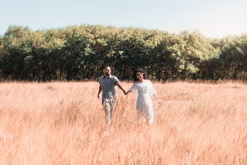 Couple Holding Hands and Walking on Meadow