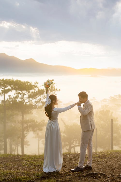 Groom Kissing the Hand of the Bride while Standing on a Hill with View of Mountains 