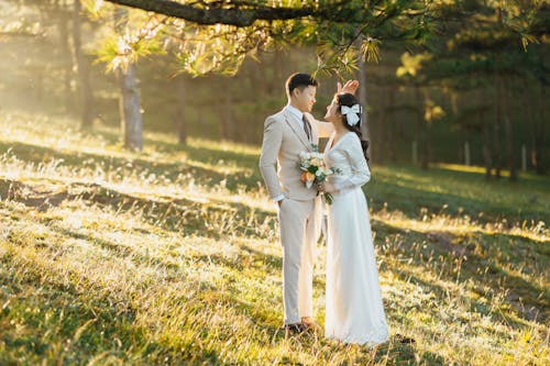 Bride and Groom Standing on a Meadow in Sunlight and Smiling 