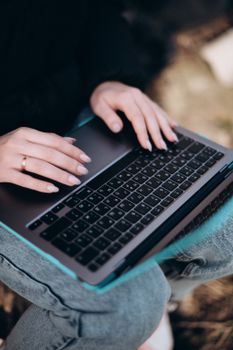 A close-up view of hands typing on a laptop outdoors, showcasing technology in a natural setting.