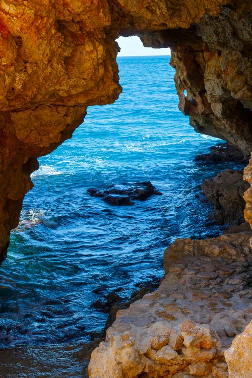 Free A stunning view of the blue ocean through a natural rock archway, perfect for summer travel inspiration. Stock Photo