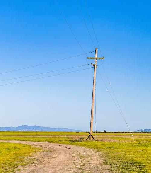 Free A scenic rural landscape featuring a telephone pole and winding dirt road under a clear blue sky. Stock Photo