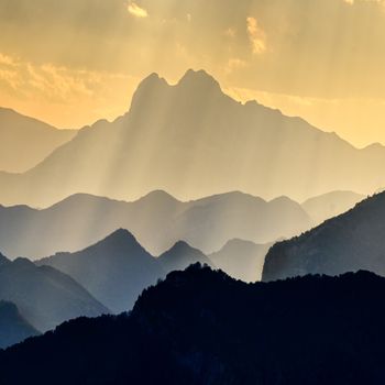 Breathtaking view of mountain silhouettes with sun rays breaking through the clouds at dusk.