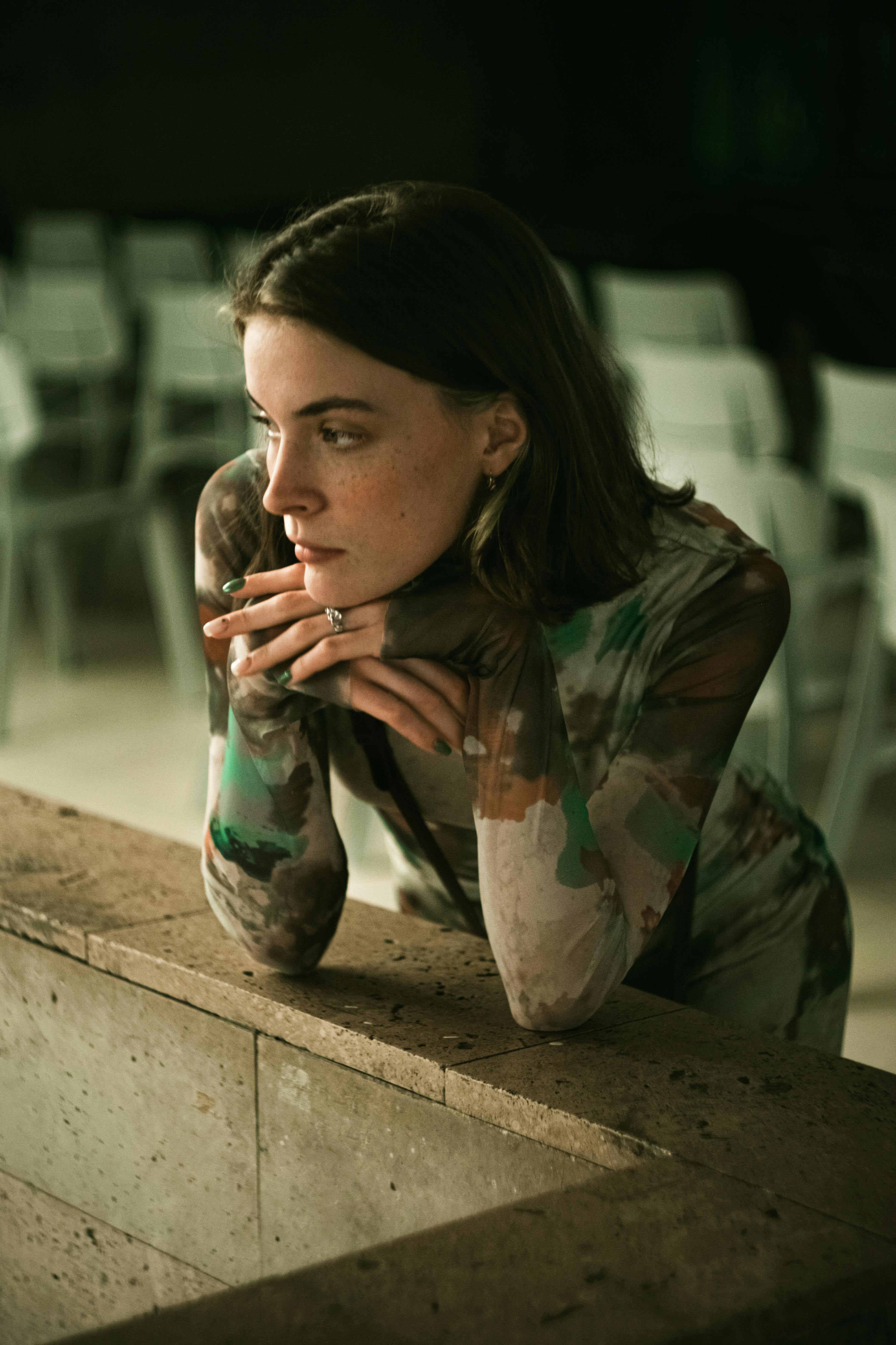 Pensive woman in a camouflage style top leaning on a stone surface indoors.