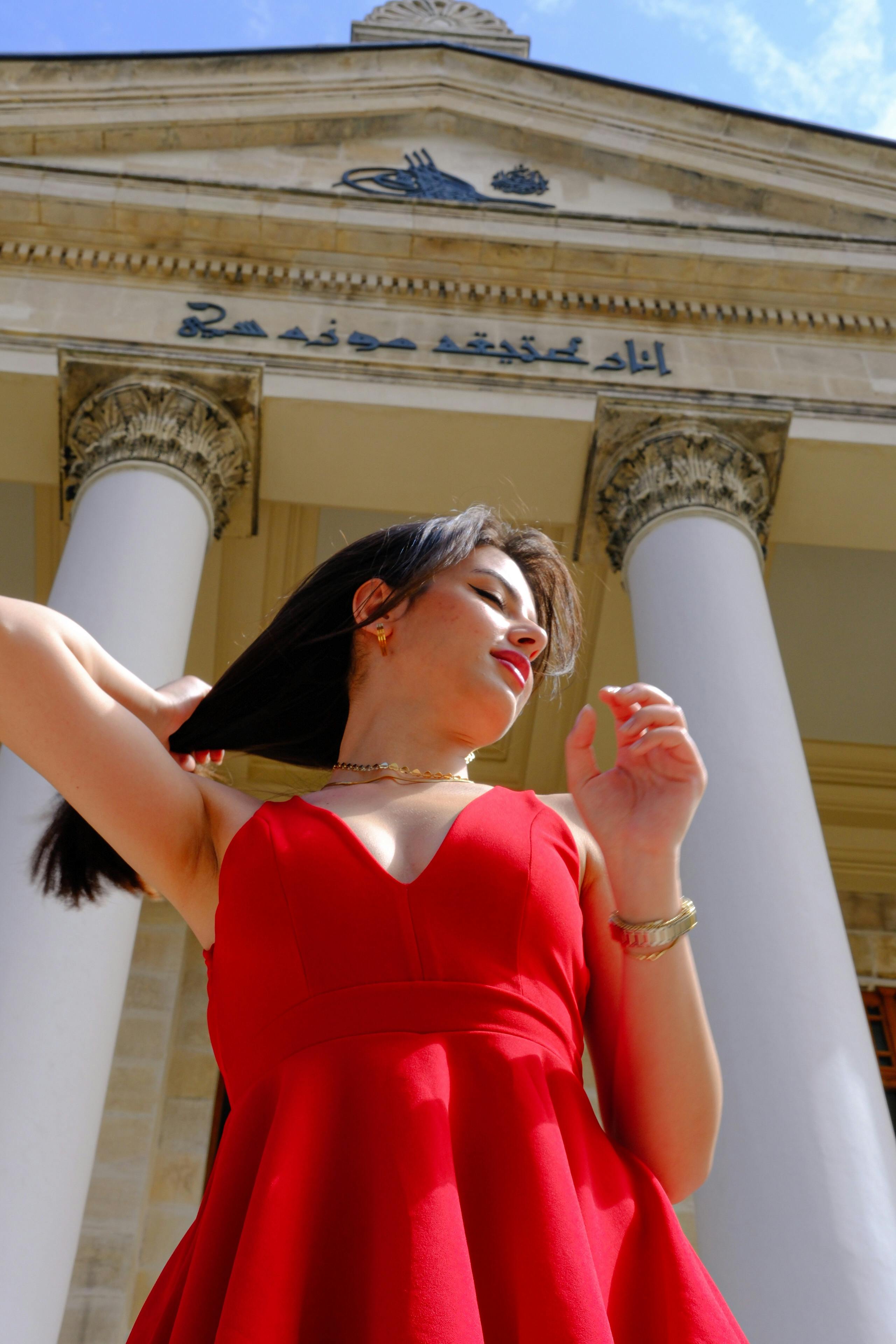 Woman in Red Dress Posing under Building with Arabic Writing and