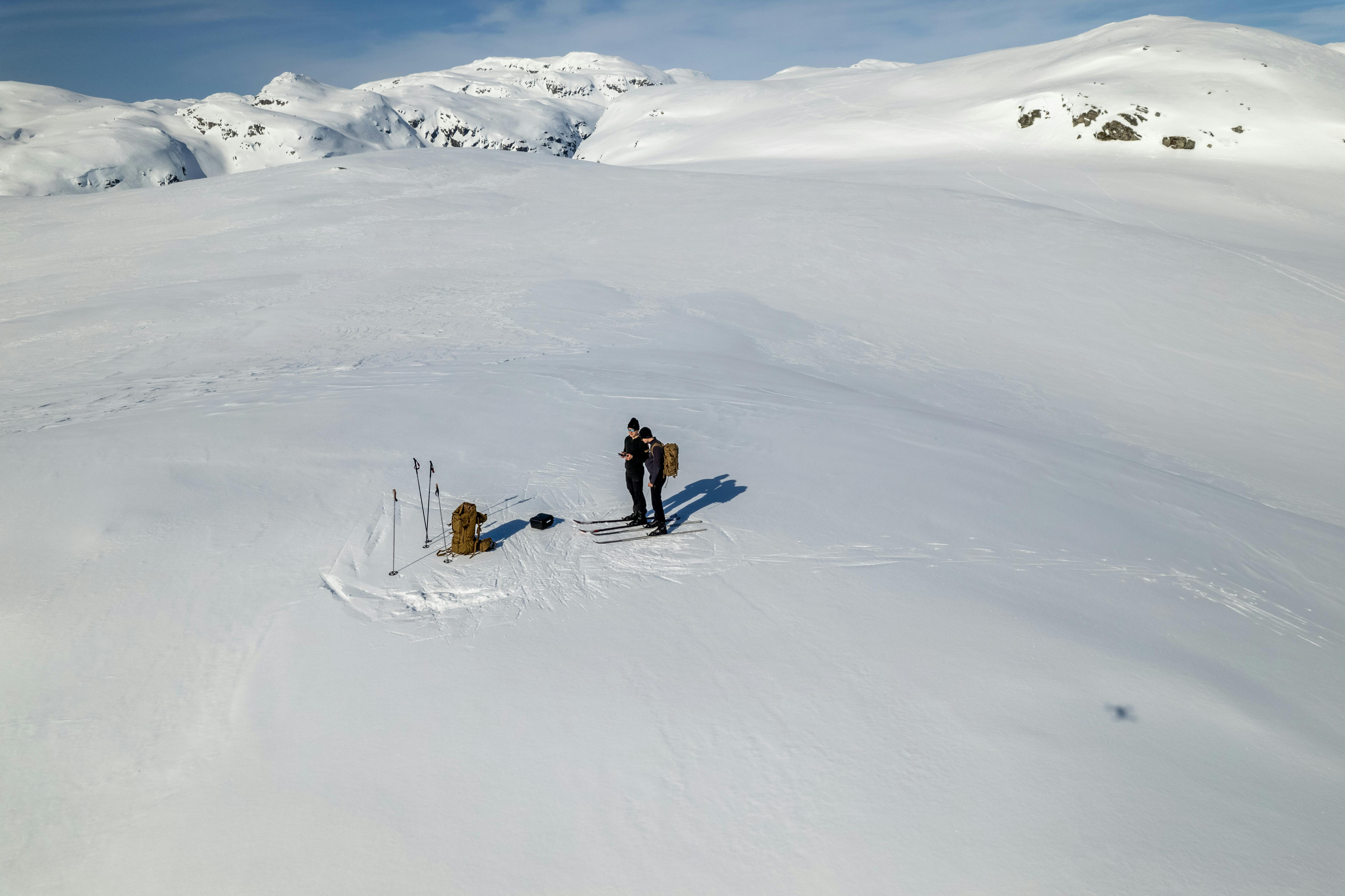 Two people skiing on a vast snowy landscape in Sauda, Norway, with distant mountains.