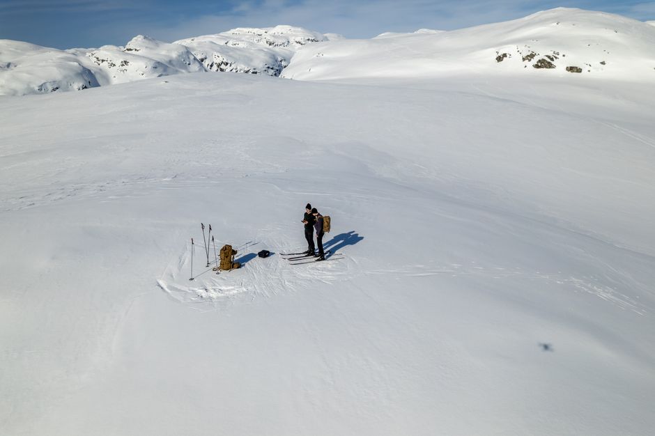 Two people skiing on a vast snowy landscape in Sauda, Norway, with distant mountains.