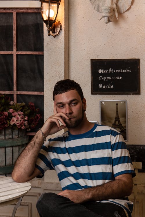 Homem Vestindo Uma Camiseta Listrada De Azul E Branco Com Gola Redonda Sentado