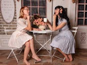 两位优雅的女士穿着复古连衣裙，在舒适的咖啡馆里惬意地聊天、喝咖啡