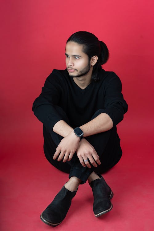 Young Man in a Black Outfit Posing in Studio on Red Background 
