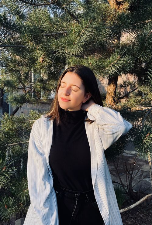 Free Portrait of a serene woman basking in sunlight amidst conifer trees in a garden. Stock Photo