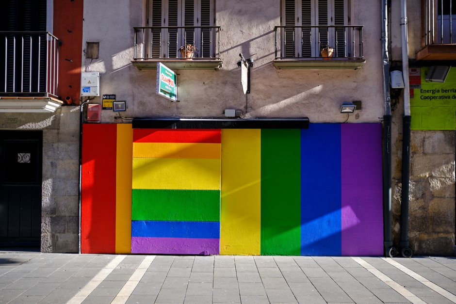 Pared vibrante pintada con los colores del arcoíris en un entorno urbano, simbolizando diversidad e inclusión.