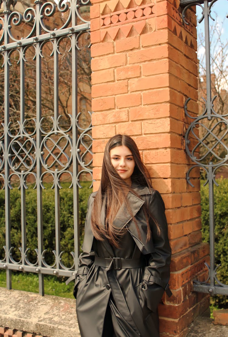 Young Woman In A Leather Coat Standing Near A Fence In City 