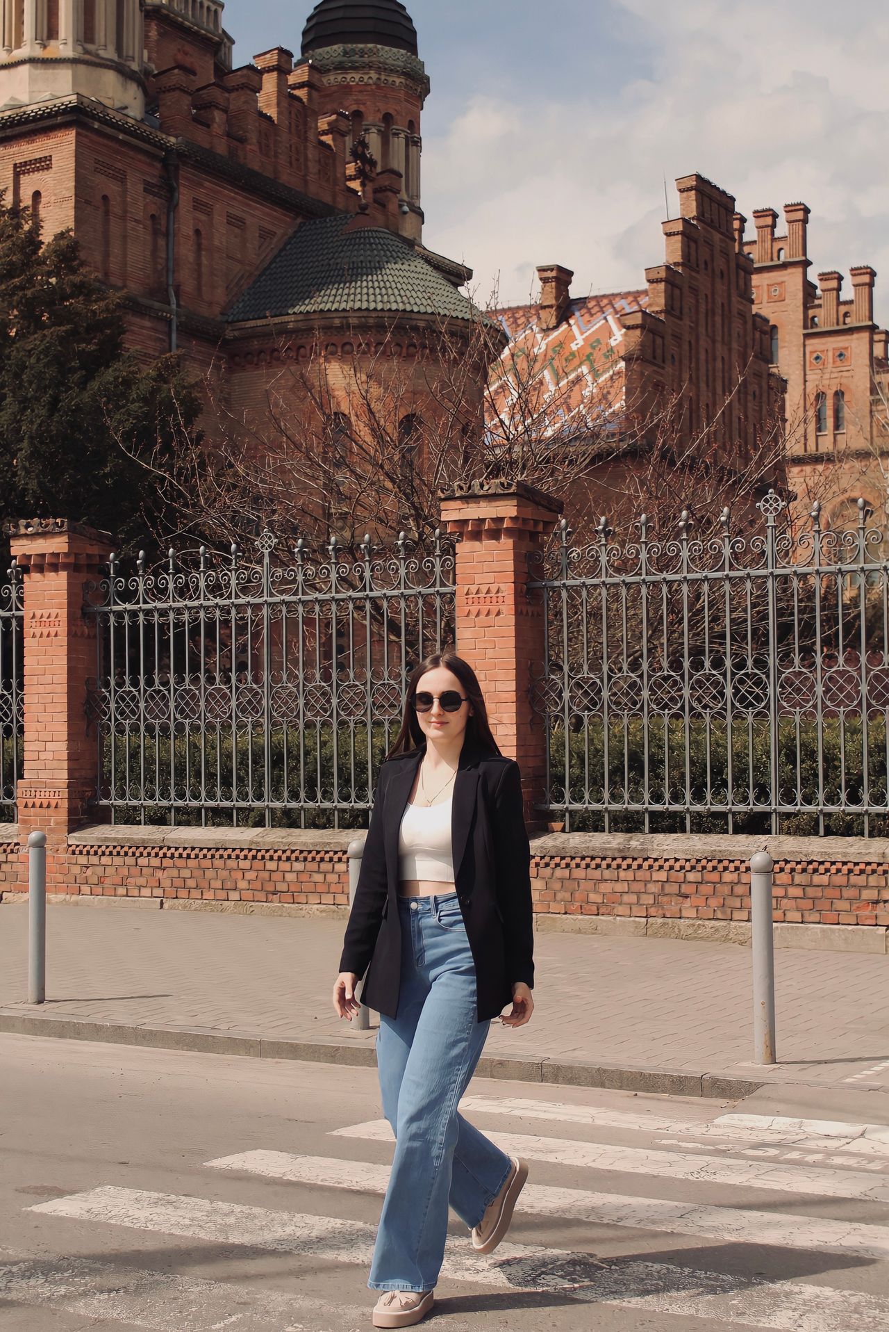 Woman in a black blazer, white top, and blue jeans crossing a street