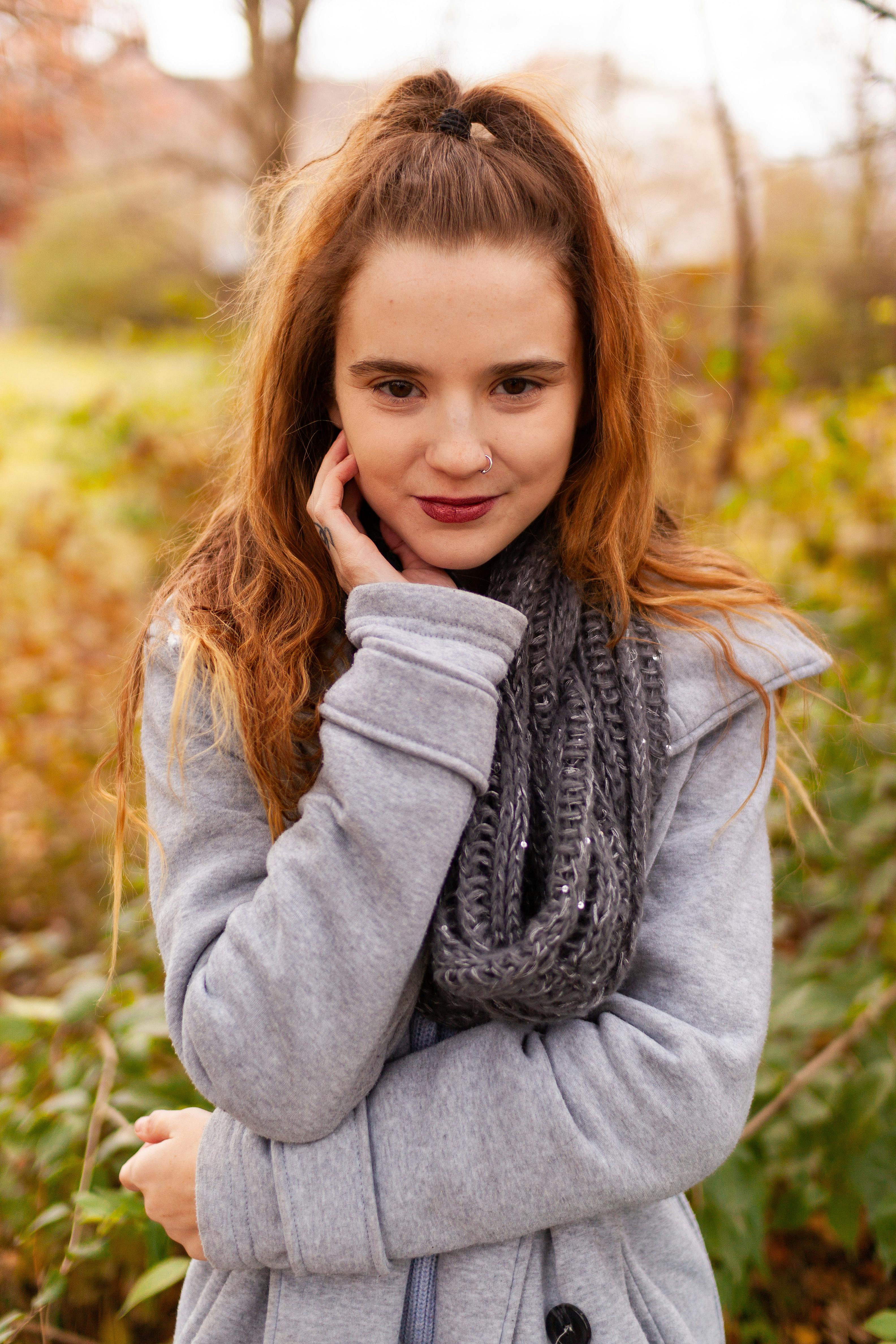 一位戴着温暖围巾和毛衣的女子，站在秋日的森林里，散发着舒适宁静的氛围