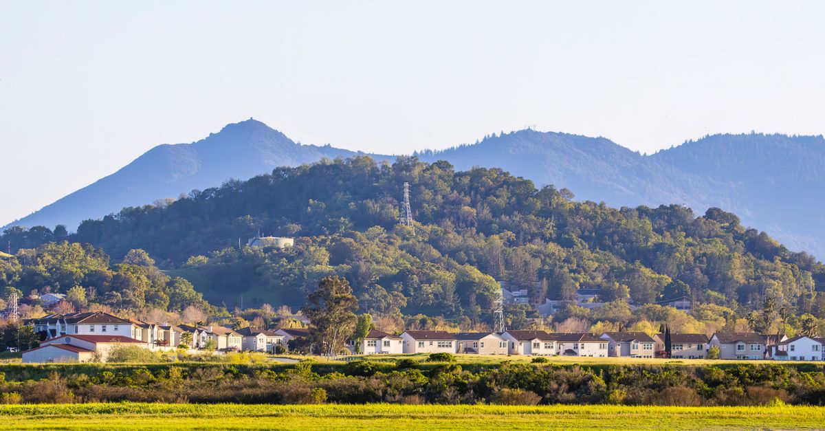 Scenic view of residential houses with lush green hills and mountains in the background.