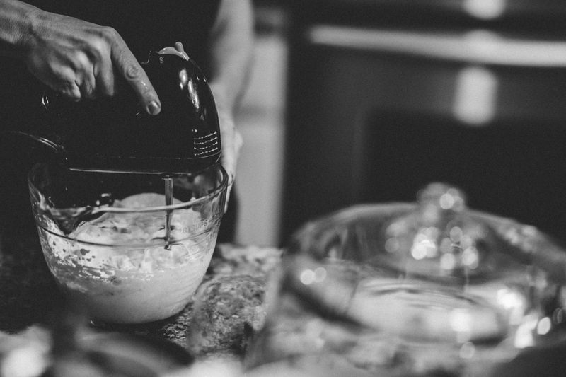 A hand using a mixer in a monochrome kitchen setting, creating a classic baking scene.
