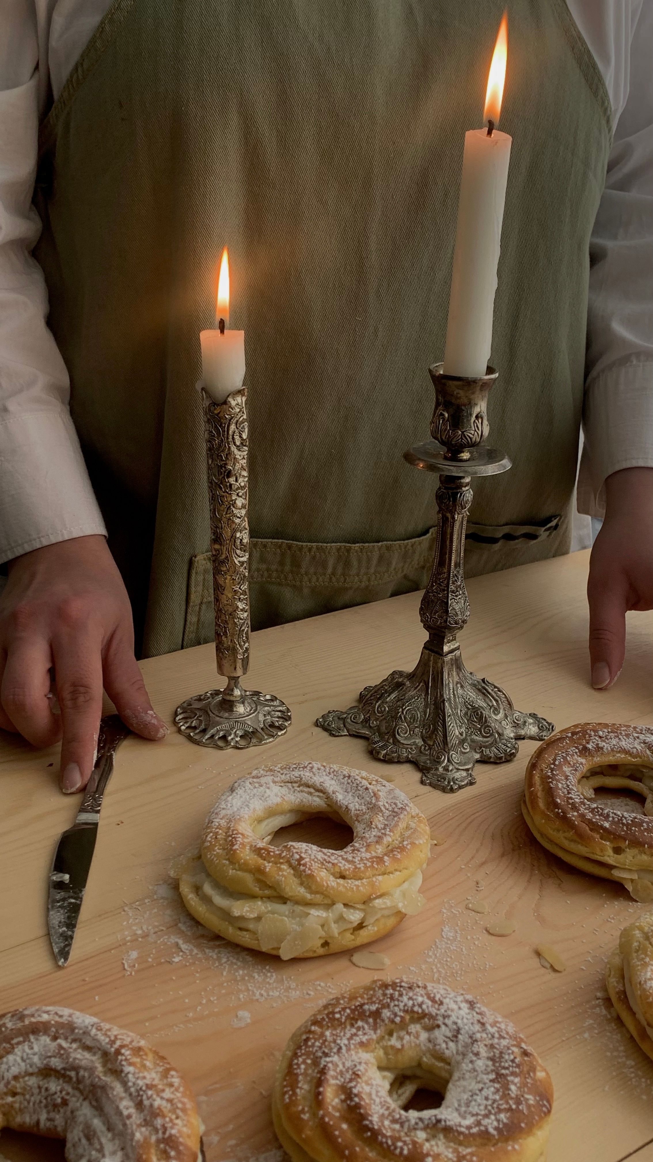 A baker arranging pastries on a table with elegant candleholders and candles, creating a cozy atmosphere.