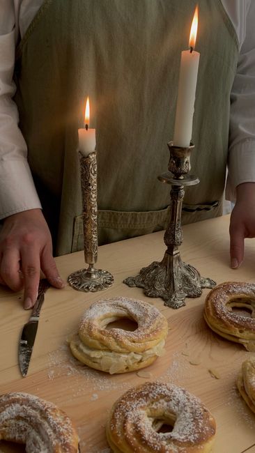 A baker arranging pastries on a table with elegant candleholders and candles, creating a cozy atmosphere.