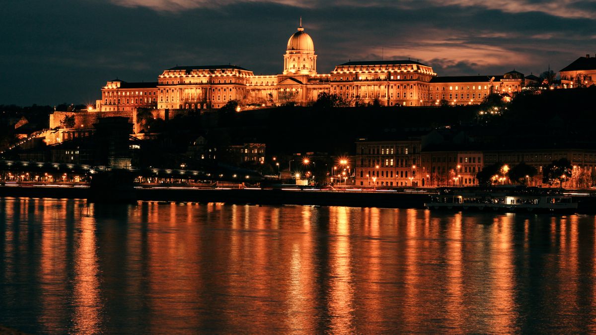 Buda Castle glowing at night, reflecting on the Danube River in Budapest, Hungary.