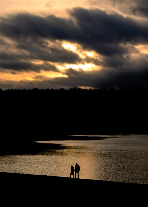 Silhouettes of People Walking near a Body of Water at Sunset