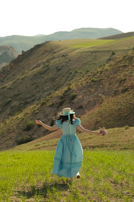 Woman wearing a blue dress and hat enjoying a summer stroll on a scenic hillside.
