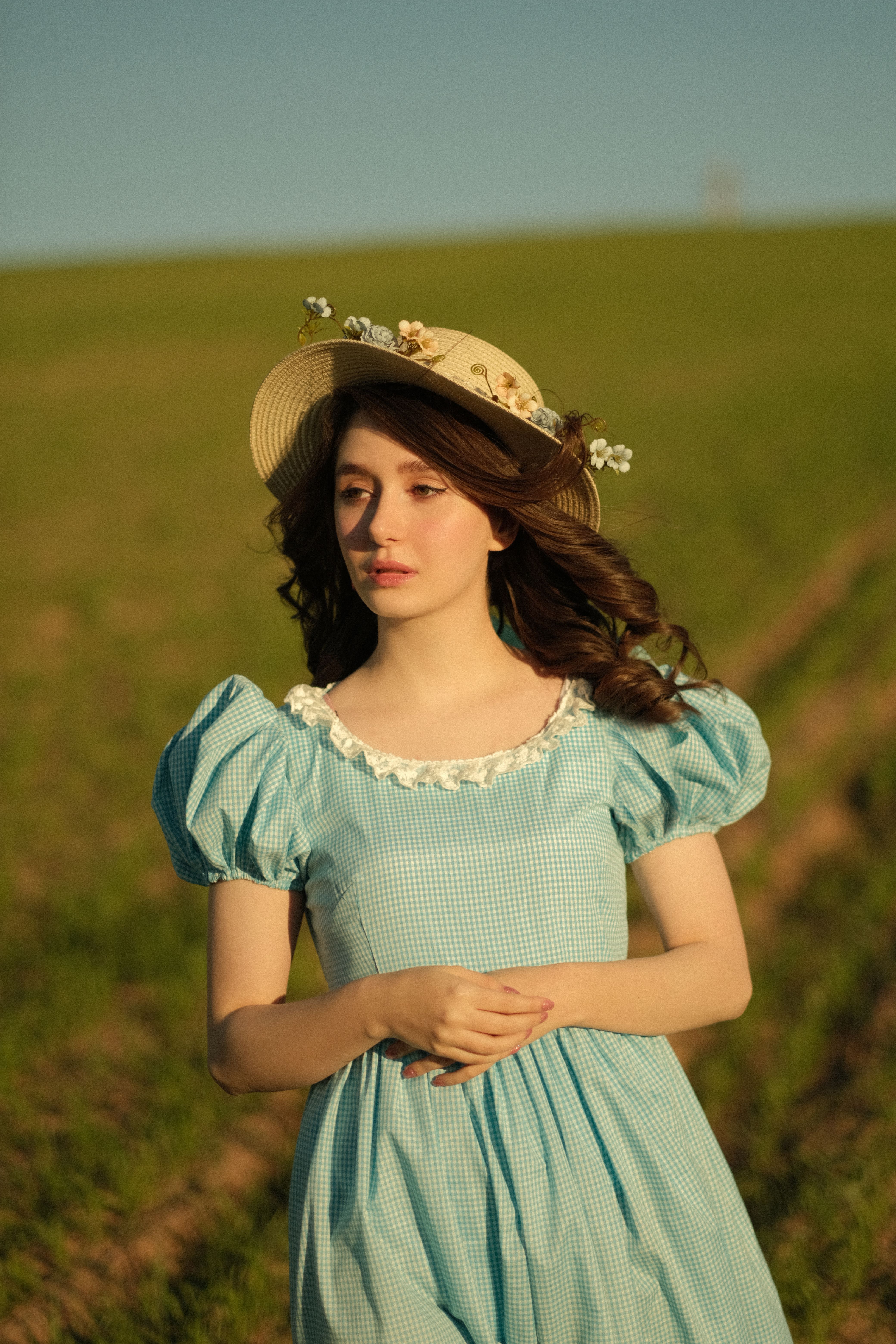 A serene portrait of a woman in a vintage blue dress and sun hat in a sunlit meadow.