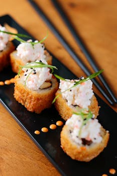 Close-up of crispy sushi rolls topped with crab salad on a black plate.
